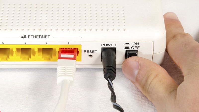 Một người đang nhấn nút nguồn để khởi động lại router WiFi.