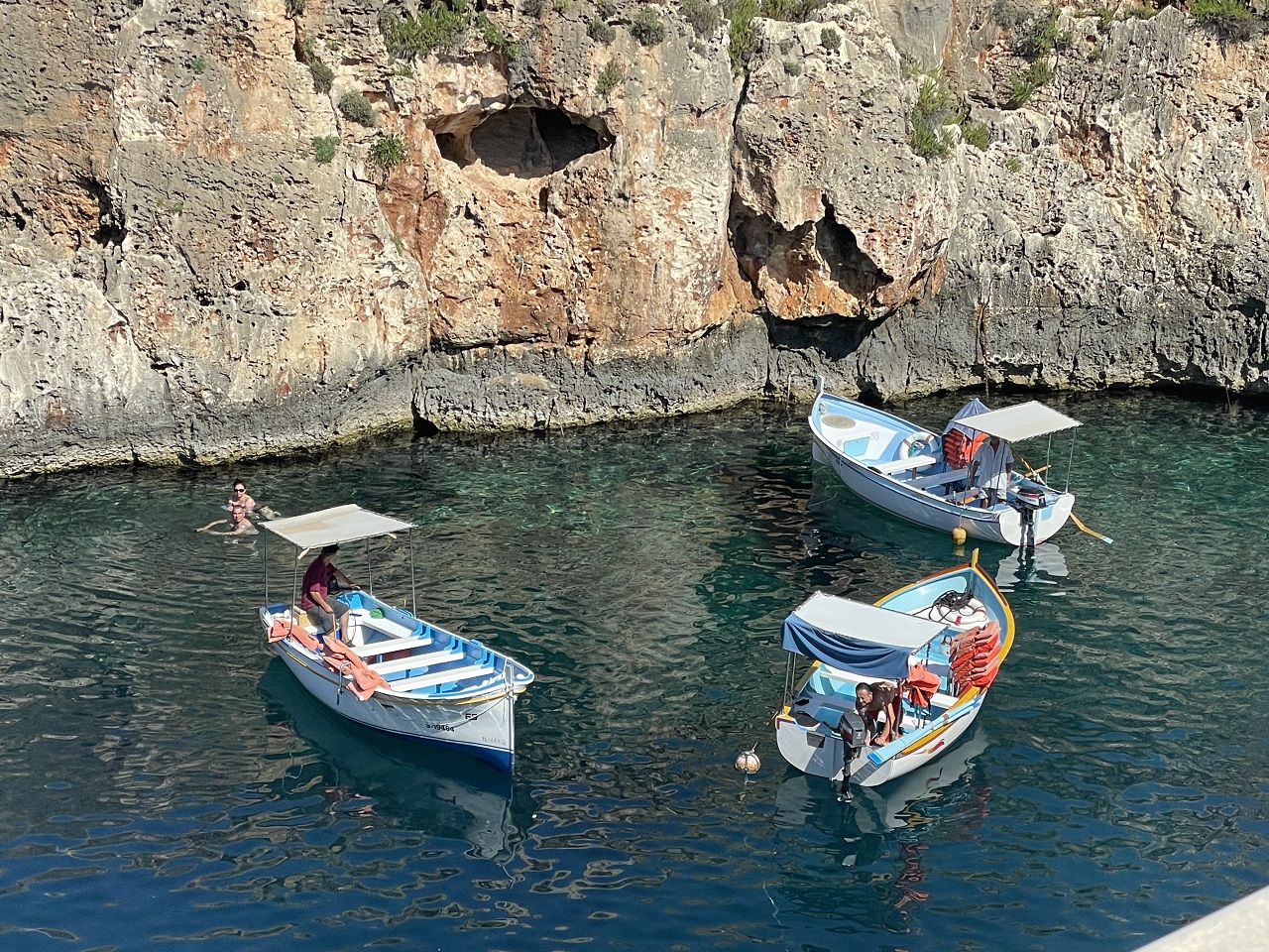 thee colorful boats in a U shape along the seaside cliffs at blue grotto