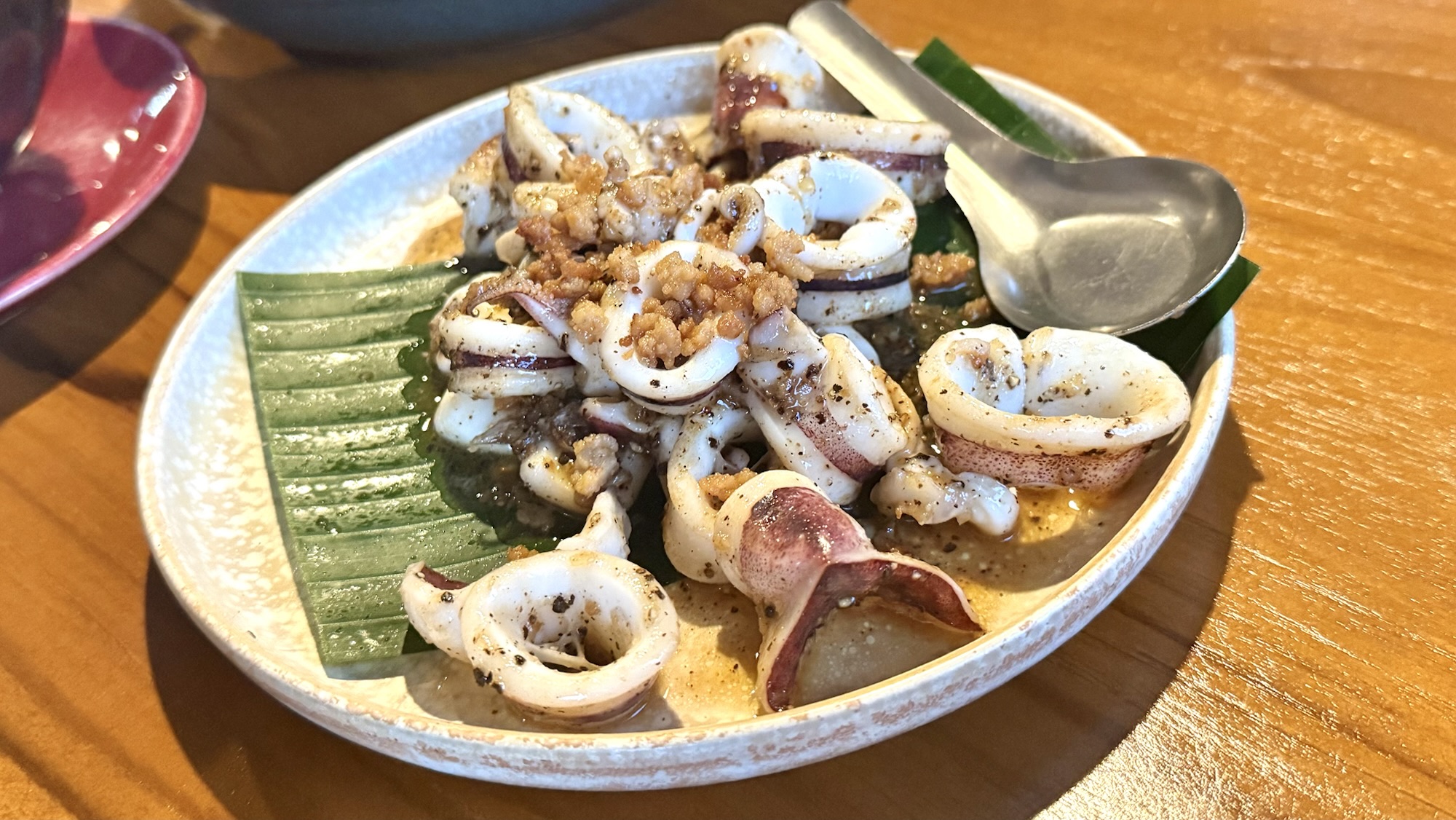 A dish of stir-fried squid garnished with crispy fried shallots, served on a banana leaf in a white plate.