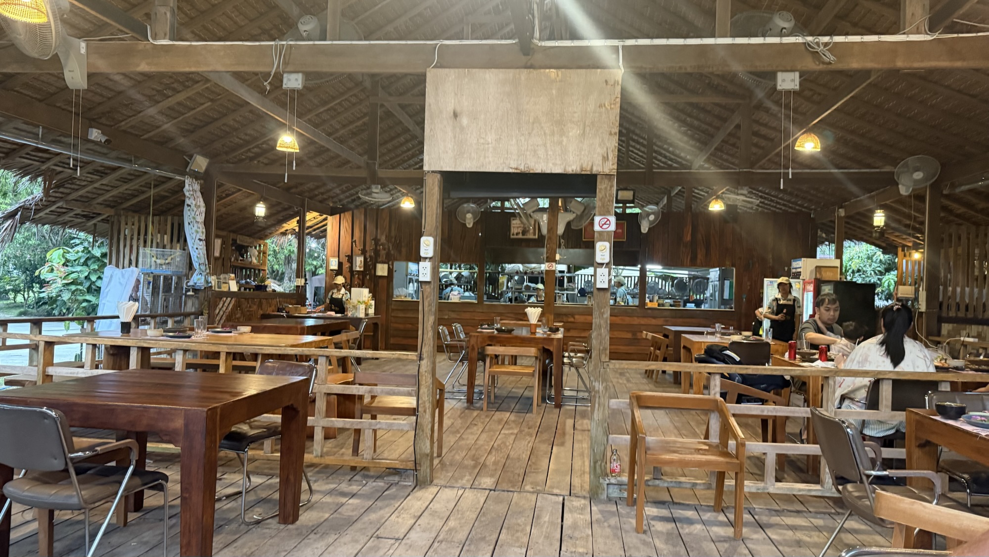 A warm and inviting interior of Ban Suan Lung Khai restaurant, featuring wooden tables and chairs, an open kitchen, and a rustic ceiling in Koh Samui, Thailand.