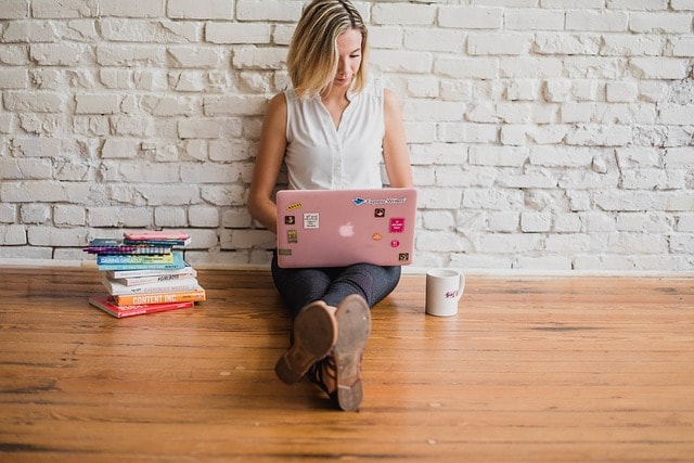 A girl sitting on a wooden floor with a laptop on her lap .