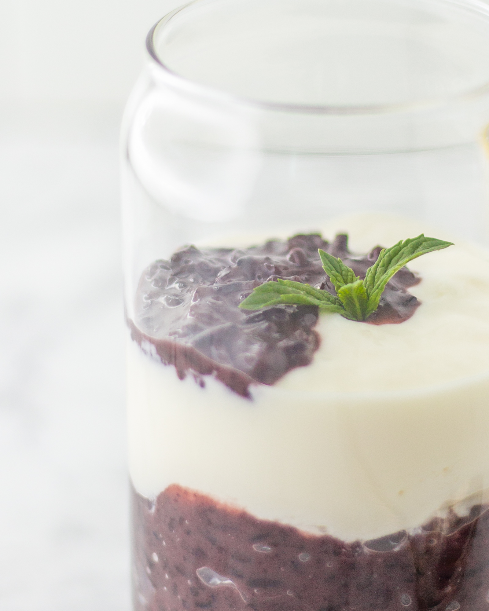 A glass filled with layers of creamy yogurt and purple sticky rice, garnished with mint leaves.